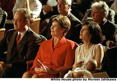 Georgetown University President John J. DeGioia, Laura Bush, and Theresa DeGioia, who is holding young J.T. DeGioia, listen to speakers at the White House Summit on Early Childhood Cognitive Development at Georgetown University. (July 26-27) White House photo by Moreen Ishikawa.