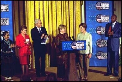 Laura Bush welcomes Ludmila Putina, wife of Vladimir Putin, President of the Russian Federation, to the Second Annual National Book Festival Saturday, October 12, 2002 in the East Room of the White House. Standing with the First Ladies on stage are, left to right, Native American poet Lucy Tapahoso, writer Mary Higgins Clark, Librarian of Congress James Billington, and NBA player Jerry Stackhouse.