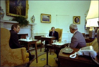While sitting in front of the fireplace in the Oval Office February 7, 1977, President Jimmy Carter hosts a lunch for Vice President Mondale and energy adviser James Schlesinger. Hanging above the mantel is Charles Willson Peale’s portrait of George Washington, which President Carter acquired for the White House’s permanent art collection.