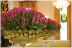 Hot pink tulips and green pears stand in line on the center table of the East Room.