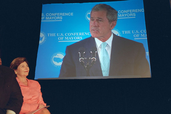 Laura Bush looks on in the audience as President George W. Bush is displayed on a giant screen monitor during his speech at the 69th Conference of Mayors in Detroit, Michigan, Monday, June 25, 2001. WHITE HOUSE PHOTO BY ERIC DRAPER