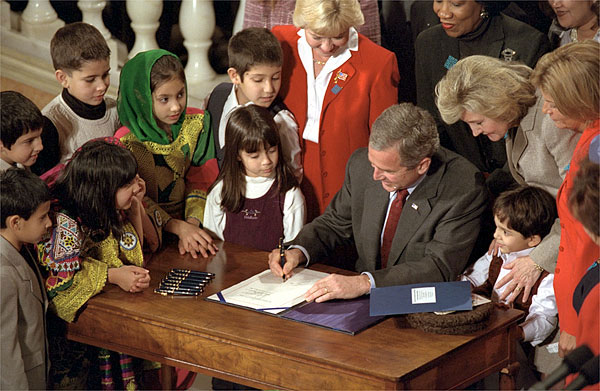 Surrounded by children, President George W. Bush signs the Afghan Women and Children Relief Act of 2001 at The National Women's Museum in the Arts Dec. 12, 2001. "The overwhelming support for this legislation sends a clear message: As we drive out the Taliban and the terrorists, we are determined to lift up the people of Afghanistan," said the President in his remarks. White House photo by Tina Hager.