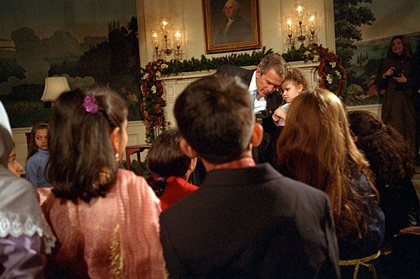 President George W. Bush takes a small break to hear what Alexandria Hudome, 3, has to say as he reads a poem to Muslim children during Eid Al-Fitr at the White House December 17, 2001. "Eid is a time of joy, after a season of fasting and prayer and reflection," said President Bush. "Each year, the end of Ramadan means celebration and thanksgiving for millions of Americans." White House photo by Tina Hager.