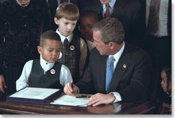 With the help from some new friends, President George W. Bush signs legislation promoting safe and stable families at the White House Jan. 17, 2002. "The legislation reaffirms our country's commitment to helping children grow up in secure and loving families by encouraging adoption," said the President during the ceremony. White House photo by Paul Morse.