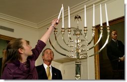 President George W. Bush watches as Daniella Wald, 12, lights one of the candles on the Menorah Wednesday, Dec 4 in the White House. President Bush presented one of the lighted candles to Daniella Wald, who lit the first three candles, and she presented the lighter candle to her sister, Alexandra Wald, 15, who lit the other three. Both of the girls are from Manhattan, and their father, Victor Wald, was killed in the Sept. 11 attacks on the World Trade Center.  White House photo by Paul Morse