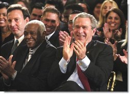 President George W. Bush applauds during the Celebration of Hispanic Heritage Month in the East Room, Thursday, Oct 2, 2003. Also pictured from left are, Tony Garza, U.S. Ambassador to Mexico and Pedro Knight, the husband of late singer Celia Cruz.  White House photo by Eric Draper