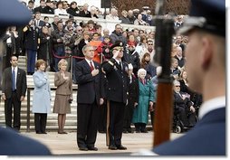 Placing his hand over his heart, President George W. Bush participates in the Wreath Laying Ceremony at the Tomb of the Unknowns in Arlington Cemetery on Veterans Day Nov. 11, 2003. Laura Bush is pictured standing behind the President.  White House photo by Paul Morse