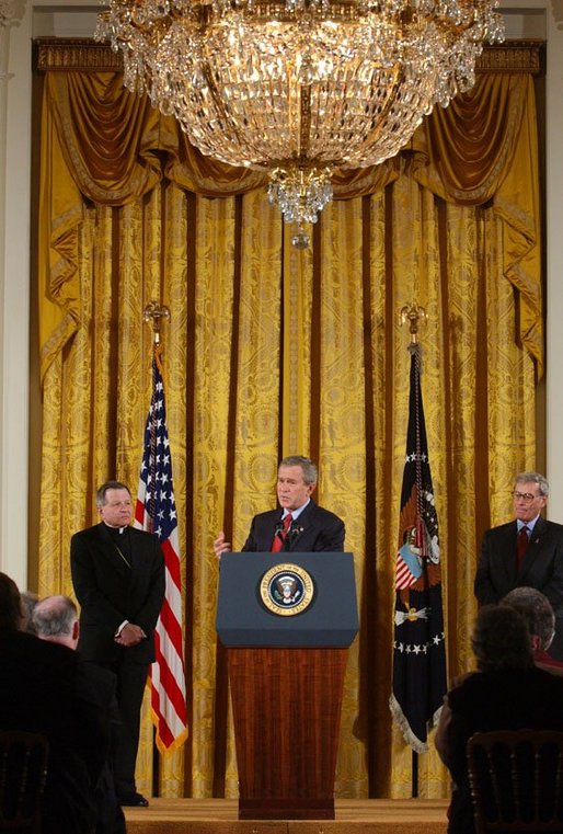 President George W. Bush addresses The National Catholic Educational Association in the East Room Friday, Jan. 9, 2004. Pictured with the President are Bishop Gregory Aymond of Austin, Texas, left and Michael Guerra, President of the NCEA. White House photo by Tina Hager