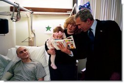 President George W. Bush reads a baby book with U.S. Army Reservist First Lieutenant Brandan Mueller of Webster Groves, Mo., his wife Amanda, and their daughter Abigail at Walter Reed Army Medical Center in Washington, D.C., Friday, March 19, 2004. Lt. Mueller was injured while serving in Operation Iraqi Freedom.  White House photo by Eric Draper