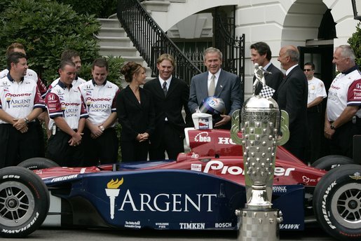 After being presented a racing helmet, President George W. Bush talks with Buddy Rice (center, left), the winner of 2004 Indianapolis 500, and his championship team, Rahal/Letterman Racing, during a visit to the South Lawn of the White House, July 19, 2004. White House photo by Paul Morse.