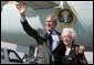 President George W. Bush waves to photographers with Freedom Corps Greeter Lucia Haas in front of Air Force One after his arriving in Phoenix, Arizona, Wednesday, Aug. 11, 2004. Hass, 73, spends two days a week as a volunteer at Surprise Senior Center in Surprise, Arizona, where she teaches English and Spanish Classes, calls Bingo games, instructs needlecraft and sewing classes and serves meals to seniors. White House photo by Eric Draper.