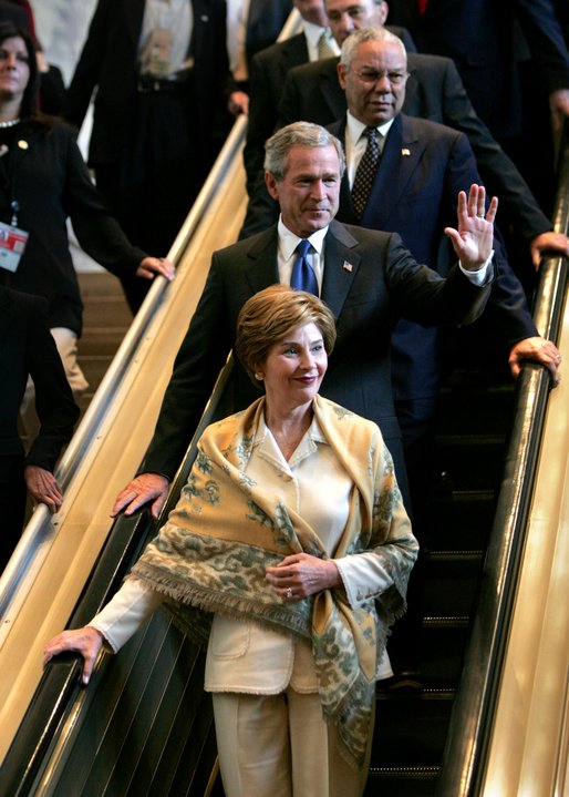 Descending the escalator with Laura Bush and Secretary of State Colin Powell, President George W. Bush waves to the international media after delivering his speech to the United Nations General Assembly in New York City Tuesday, Sept. 21, 2004. White House photo by Eric Draper.