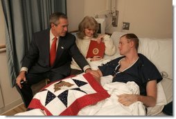 President George W. Bush visits with USMC Lance Corporal Sean Phillips and his mother, Sharon, at the National Naval Medical Center in Bethesda, Md., Saturday, Dec. 11, 2004. Cpl. Phillips was injured in Operation Iraqi Freedom. While recovering in Germany, he received a donated quilt from supporters in Texas. Given to wounded soldiers returning to the states, the quilts come from groups and individuals from all over America. The President added his own Texas signature to the quilt. White House photo by Paul Morse