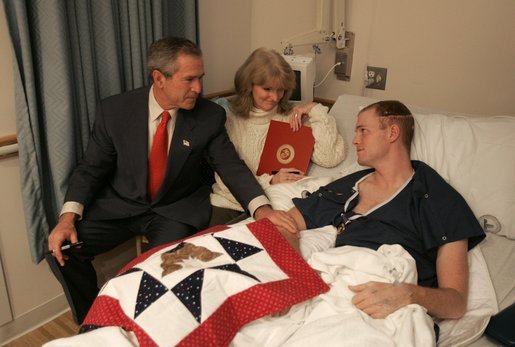 President George W. Bush visits with USMC Lance Corporal Sean Phillips and his mother, Sharon, at the National Naval Medical Center in Bethesda, Md., Saturday, Dec. 11, 2004. Cpl. Phillips was injured in Operation Iraqi Freedom. While recovering in Germany, he received a donated quilt from supporters in Texas. Given to wounded soldiers returning to the states, the quilts come from groups and individuals from all over America. The President added his own Texas signature to the quilt.White House photo by Paul Morse