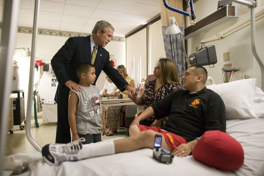 President George W. Bush holds the hand of Elvira Flores, wife of Lance Cpl. Alberto Flores, as their son A.J., watches during the President's visit Friday, July 1, 2005, to Walter Reed Army Medical Center. Lance Cpl. Flores, from Salinas, Calif., is being treated for injuries received while serving in Operation Iraqi Freedom. White House photo by Eric Draper