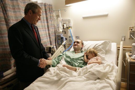 President George W. Bush shakes hands with Sgt. Jacob Knospler of Stroudsburg, Pa., as the Marine's 10-month-old daughter Jahna sleeps next to her dad at the National Naval Medical Center in Bethesda, Md. Saturday, July 30, 2005. Sgt. Knospler is recovering from injuries suffered while serving in Operation Iraqi Freedom. White House photo by Eric Draper