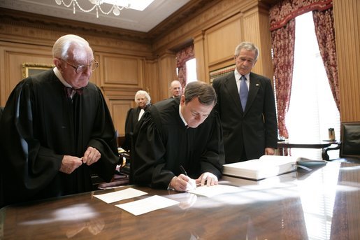 President George W. Bush looks on as U.S. Supreme Court Chief Justice John Roberts signs documents during his investiture ceremony at the U.S. Supreme Court, Monday, Oct. 3, 2005 in Washington. Associate Justice John Paul Stevens is seen at left, and Associate Justices Sandra Day O'Connor and Anthony Kennedy, background. White House photo by Eric Draper
