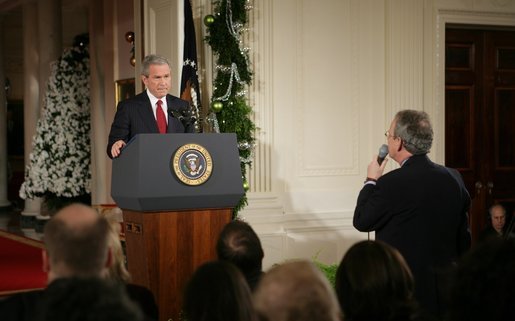 President George W. Bush listens as Terrence Hunt of The Associated Press delivers a question Monday, Dec. 19, 2005, during the President's press conference in the East Room of the White House. In response to Mr. Hunt's question, the President responded, "We're at war, and we must protect America's secrets." White House photo by Paul Morse