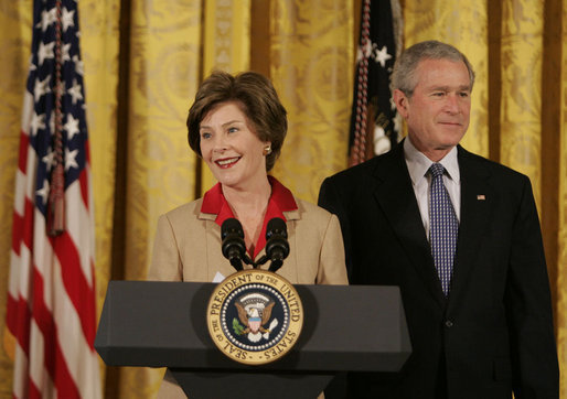 President George W. Bush listens on as Mrs. Laura Bush welcomes women leaders to the East Room for a celebration Tuesday, March 7, 2006, of International Women's Day. Mrs. Bush said, "I've been privileged to meet thousands of women from many nations, and I believe that women everywhere share the same dreams -- to be educated, to live in peace, to enjoy good health, to be prosperous, and to be heard." White House photo by Kimberlee Hewitt