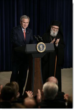President George W. Bush is applauded by Archbishop Demetrios from the Greek Orthodox Church of America, Friday, March 24, 2006 at the Eisenhower Executive Office Building in Washington, where President Bush addressed an audience celebrating Greek Independence Day and honored the 185th anniversary of Greece's Independence.  White House photo by Eric Draper