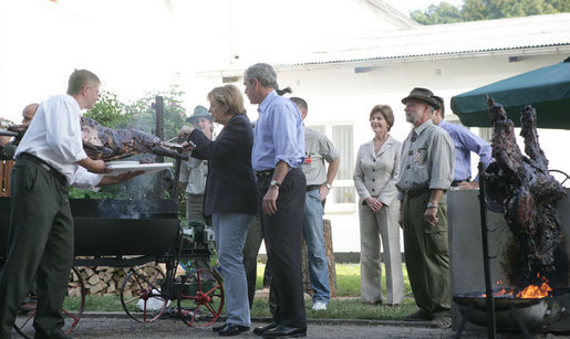 As President George W. Bush and Laura Bush look on, German Chancellor Angela Markel slices up some barbeque Thursday, July 13, 2006, during dinner in Trinwillershagen, Germany. The Bushes continue their Europe trip when they depart Germany Friday en route to Russia and the G8 Summit. White House photo by Shealah Craighead