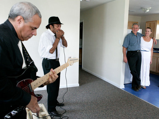 President George W. Bush stands with Polly Noble as they listen Tuesday, Aug. 29, 2006, to J.D. Hill on his harmonica and guitarist Charlie Moore during a visit to Musicians' Village in New Orleans' 9th Ward. The President and Laura Bush hosted a lunch with volunteers from Habitat for Humanity in appreciation of their work on the site for displaced New Orleans musicians. White House photo by Eric Draper