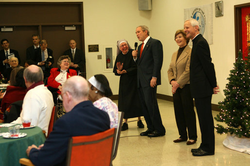 President George W. Bush draws smiles from the audience of volunteers, staff and residents at the Little Sisters of the Poor Tuesday, Dec. 18, 2007, during a visit with Mrs. Laura Bush to the Washington, D.C. facility. Enjoying the moment with them are Mother Benedict de la Passion, Superior and President of Little Sisters of the Poor, and Archbishop Donald Wuerl of the Archdiocese of Washington. White House photo by Shealah Craighead