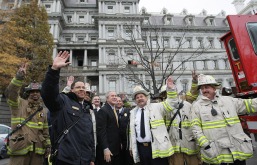 President George W. Bush joins firefighters from the District of Columbia as they wave to the media Wednesday after fighting a fire in the Eisenhower Executive Office Building on the White House complex. The charred, second-floor window frame can be seen in the upper middle of the photo. White House photo by Eric Draper
