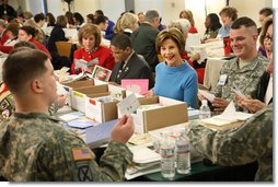 Mrs. Laura Bush joins military and civilian volunteers Saturday, Dec. 6, 2008, as she signs and sorts seasonal cards written for U.S. troops at the American Red Cross Holiday Mail for Heroes event. Seated next to Mrs. Bush at Red Cross headquarters in Washington, D.C., is young volunteer Tre'shaad "Tre" Cox, age 11, with American Red Cross President and CEO Gail McGovern at the end of the table, in red. At very far right is Bonnie McElveen-Hunter, Chairman of the American Red Cross. In the room full of volunteers, Mrs. Bush reminded Americans that they have until December 10th to send a holiday card at designated post office boxes for the troops deployed around the world.  White House photo by Chris Greenberg