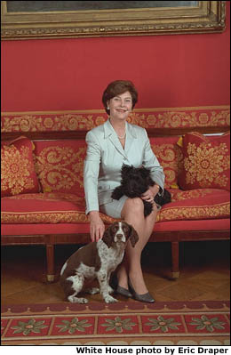 Laura Bush is seated on a red sofa with dogs Barney and Spotty. White House photo by Eric Draper.