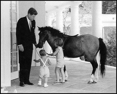 President John F. Kennedy (1961-63) spends some time at the White House with his children, Caroline and John Jr., and their pony, Macaroni. 