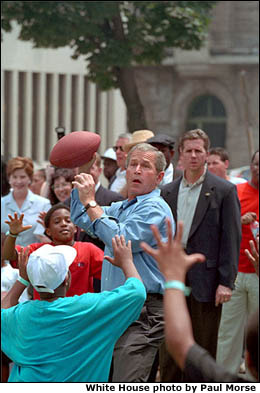 With the Secret Service watchful for any illegal moves, the President looks for an opening to throw a perfect spiral pass during a neighborhood game of street football July 4, 2001. White House photo by Paul Morse