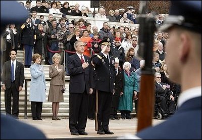 Placing his hand over his heart, President George W. Bush participates in the Wreath Laying Ceremony at the Tomb of the Unknowns in Arlington Cemetery on Veterans Day Nov. 11, 2003. Laura Bush is pictured standing behind the President.