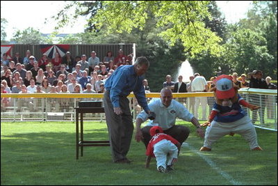 President George W. Bush and Commissioner Cal Ripken signal a "safe" for a player who took an unplanned slide as he ran toward them for his courtesy baseball and photo after the game Sunday, May 5, 2002.