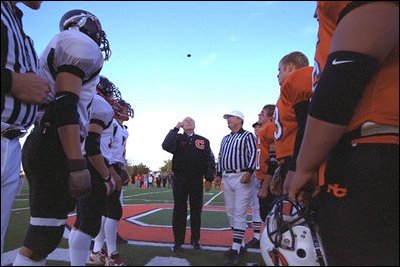 Vice President Dick Cheney flips a coin to begin the homecoming football game between the Natrona County High School Mustangs, right, and Cheyenne Central High School Indians, left, in Casper, Wyo., Sept. 20, 2002. The Mustangs won the game 24-6.