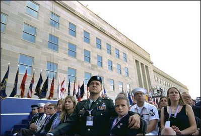 Sitting in front of the rebuilt section of the Pentagon, service personnel and families listen to President George W. Bush at the Pentagon Observance Wednesday, Sept. 11, 2002. "One year ago, men and women and children were killed here because they were Americans. And because this place is a symbol to the world of our country's might and resolve," said the President. "Today, we remember each life. We rededicate this proud symbol and we renew our commitment to win the war that began here."