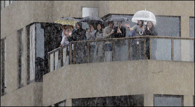 Spectators shelter themselves from a bitter rain Thursday, Sept. 6, 2007, as they wave to a motorcade carrying President George W. Bush through the streets of Sydney.
