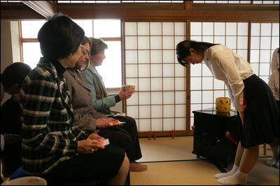 Mrs. Laura Bush accepts a cup of tea from a student in the Tea Ceremony Classroom at Doshisha Girls Junior High School and Senior High School during her visit Wednesday, Nov. 16, 2005, to Kyoto, Japan. With Mrs. Bush are Susanne Schieffer, wife of U.S. Ambassador Thomas Schieffer, and Mrs. Hanayo Kato, wife of Japanese Ambassador Ryozo Kato.