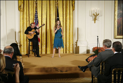 El Presidente George W. Bush, sentado al frente a la derecha, escucha la presentación de la cantante Ana Cristina y el guitarrista Marco Linares, el viernes, 6 de octubre de 2006, en el East Room de la Casa Blanca, durante la celebración del Mes de la Hispanidad. Foto por Paul Morse de la Casa Blanca