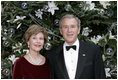 President George W. Bush and Laura Bush stand before the White House Christmas tree in the Blue Room of the White House. In keeping with this year's theme, "All Things Bright and Beautiful!" the Fraser fir is decorated with fresh white lilies.