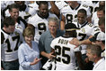 President George W. Bush and Laura Bush are surrounded by members of the New Orleans Saints football team Tuesday, Aug. 29, 2006, as they point out the name of Saints star rookie running back Reggie Bush, when the team met President Bush at the New Orleans Airport to pose for a team photo.