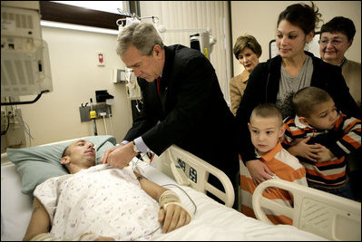 President George W. Bush presents a Purple Heart to Sgt. John Kriesel of Twin Cities, Minn., during a visit Friday, Dec. 22, 2006, to Walter Reed Army Medical Center where the National Guardsman is recovering from injuries suffered in Operation Iraqi Freedom. Looking on with Mrs. Laura Bush is Sgt. Kriesel's wife, Katie, holding their 4-year-old son Broden and 5-year-old son Elijah.