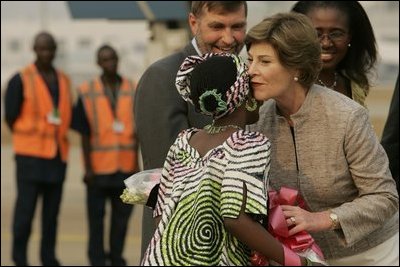 Mrs. Laura Bush embraces 11-year-old Jamila Ahmed after she presented flowers to Mrs. Bush, Tuesday, Jan. 17, 2006, upon her arrival to Abuja, Nigeria. Deputy Chief of U.S. Mission Thomas Fuery and Nigeria's Minister of Education Chinwe Obaji, are seen in the background.