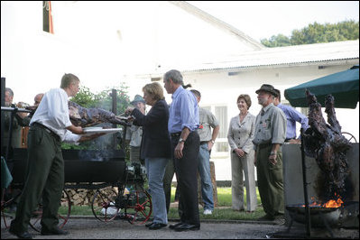 As President George W. Bush and Laura Bush look on, German Chancellor Angela Markel slices up some barbeque Thursday, July 13, 2006, during dinner in Trinwillershagen, Germany. The Bushes continue their Europe trip when they depart Germany Friday en route to Russia and the G8 Summit.
