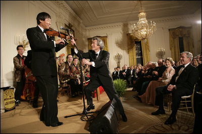 President George W. Bush watches as Japanese Prime Minister Junichiro Koizumi adjusts the microphone for country music entertainer Shoji Tabuchi Thursday evening, June 29, 2006 in the East Room of the White House, during the entertainment following the official dinner in honor of Koizumiís visit to the United States.