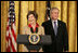 President George W. Bush listens on as Mrs. Laura Bush welcomes women leaders to the East Room for a celebration Tuesday, March 7, 2006, of International Women's Day. Mrs. Bush said, "I've been privileged to meet thousands of women from many nations, and I believe that women everywhere share the same dreams -- to be educated, to live in peace, to enjoy good health, to be prosperous, and to be heard."