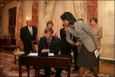 Mrs. Laura Bush, along with family of Ambassador Mark Dybul, watch as U.S. Secretary of State Condoleezza Rice assists newly sworn-in Ambassador Mark Dybul as he signs appointment documents Tuesday, October 10, 2006, during the swearing-in ceremony of Ambassador Mark Dybul in the Benjamin Franklin Room at the US Department of State in Washington, D.C.
