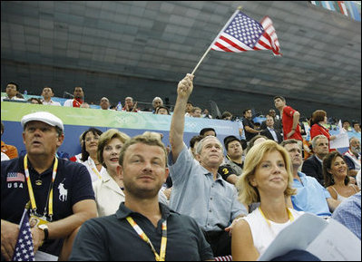 President George W. Bush, accompanied by Mrs. Laura Bush, waves an American flag as he cheers for the U.S. Olympic swimming team Monday, Aug. 11, 2008, in the National Aquatic Center at the 2008 Summer Olympic Games in Beijing.