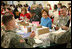Mrs. Laura Bush is seated between volunteers Master Tre'shaad Cox, 11, left, and U.S. Army Sgt. Thomas Griffin, an out-patient at Walter Reed Army Medical Center, during a visit Saturday, Dec. 6, 2008, to the American Red Cross Holiday Mail for Heroes Packing Event at the Red Cross National Headquarters in Washington, D.C. Mrs. Bush reminded the volunteers that during this holiday season, "we are reminded of our many blessings, especially our freedom. The American Red Cross Holiday Mail for Heroes project, in partnership with Pitney Bowes, provides citizens an opportunity to send holiday cards to members of our Armed Forces. I am grateful to the many volunteers gathered here today to ensure our military receives our message of thanks for the sacrifice they make each day to defend our freedom."