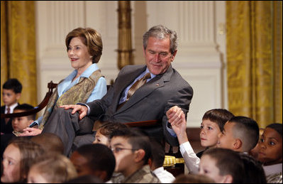 President George W. Bush, sitting with Mrs. Laura Bush, reaches to hold the hand of a young child Monday, Dec. 8, 2008 in the East Room of the White House, during the Children's Hoilday Reception and Performance.